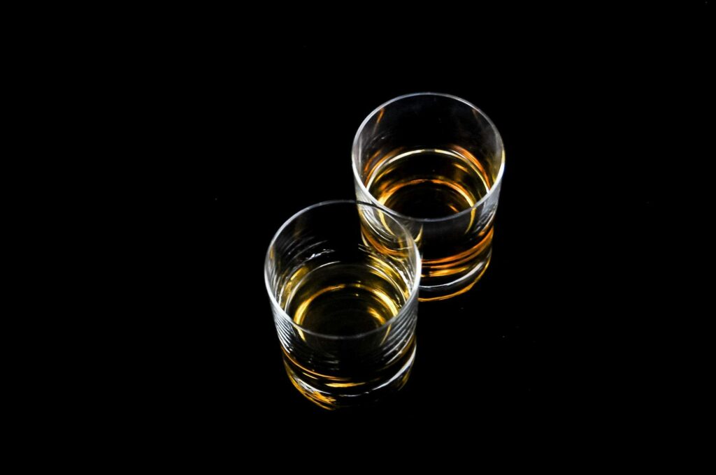 Two whiskey glasses with amber liquid reflecting on a glossy black surface.