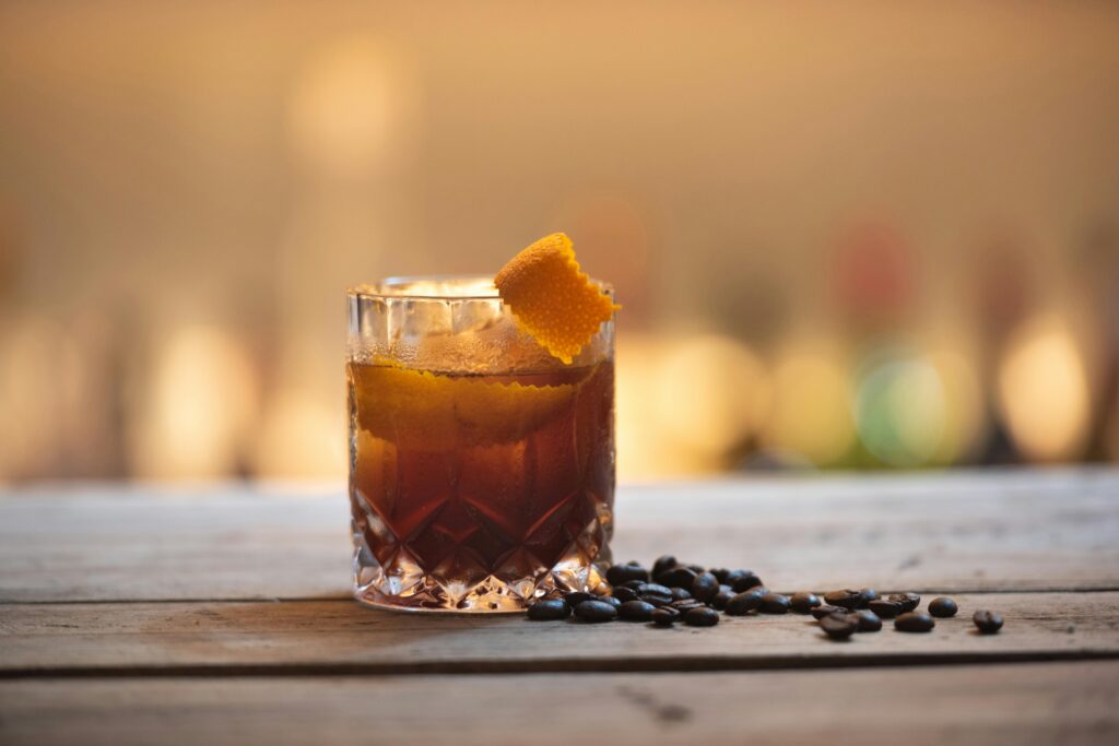 Close-up of a cocktail with orange peel and coffee beans on a rustic table.