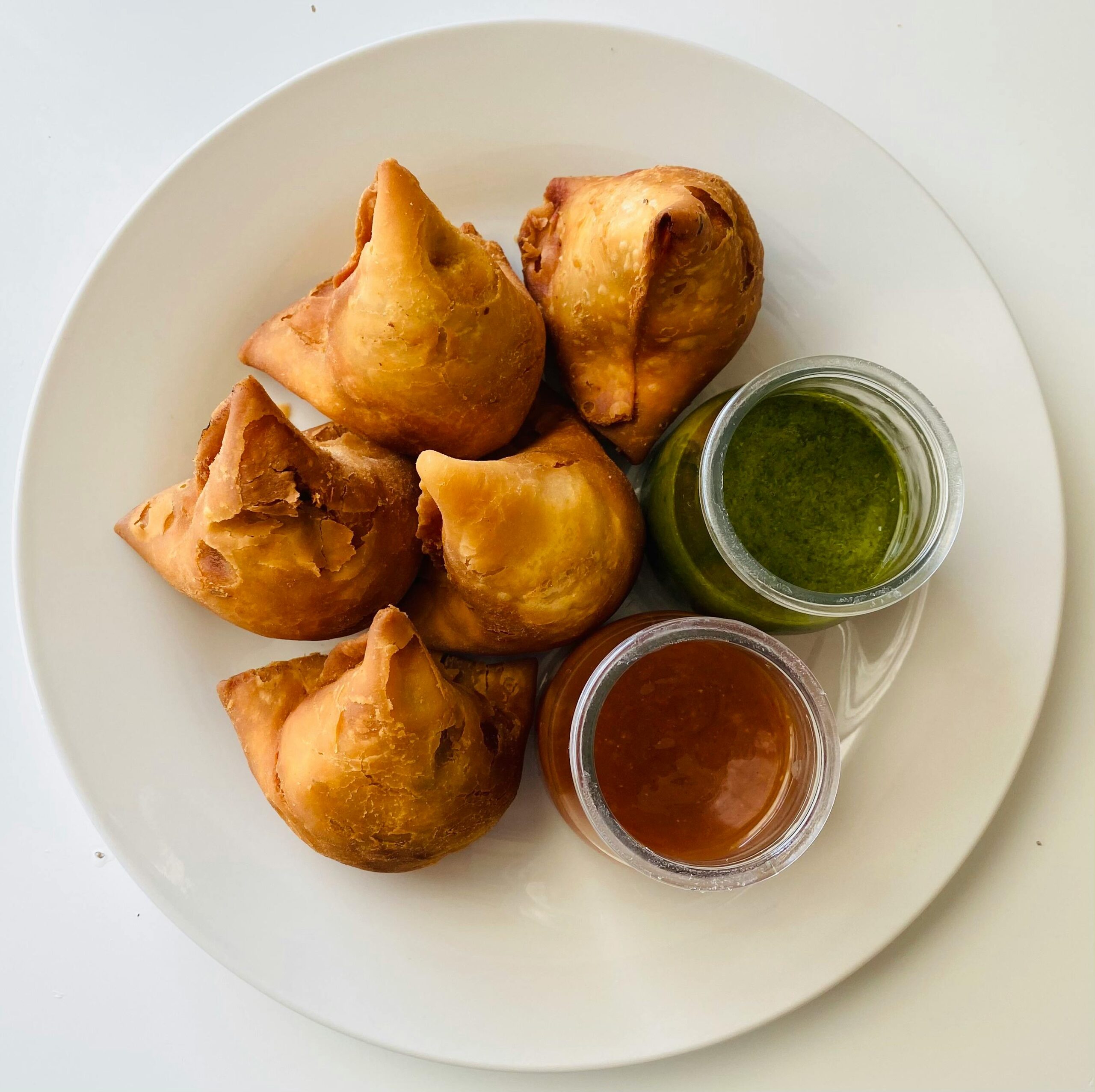 Top view of crispy samosas served with green and tamarind chutneys on a white plate.